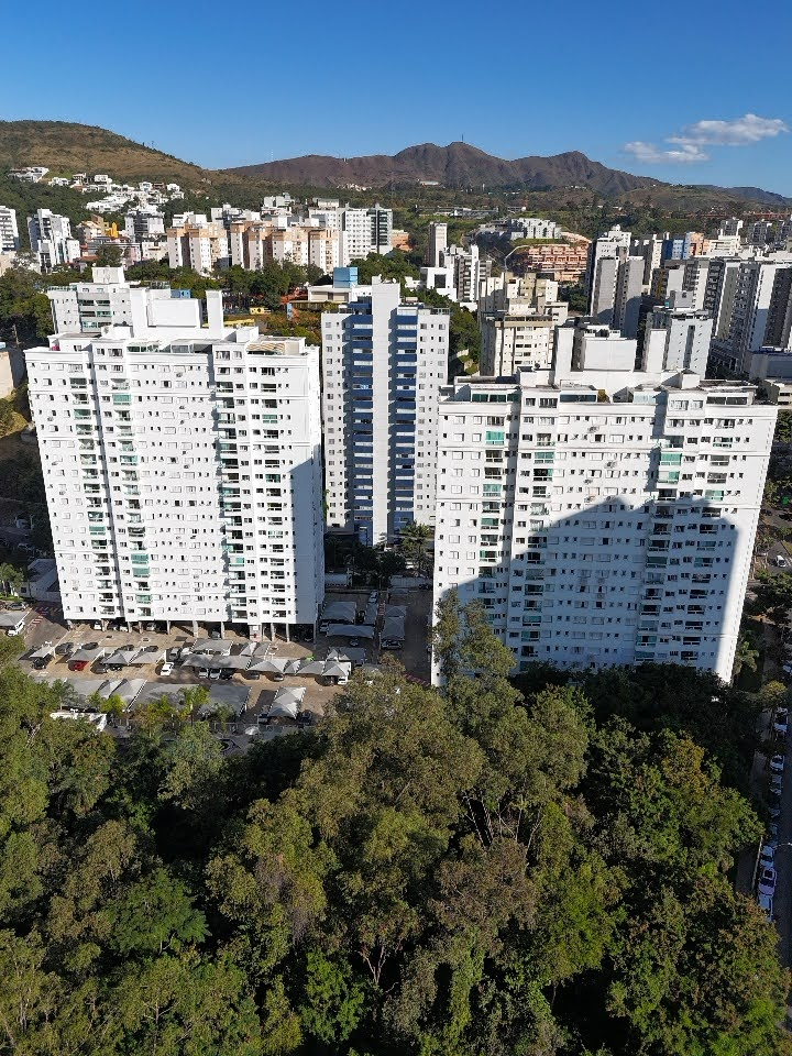 Vista aérea de edifícios residenciais brancos cercados por vegetação densa, com montanhas ao fundo