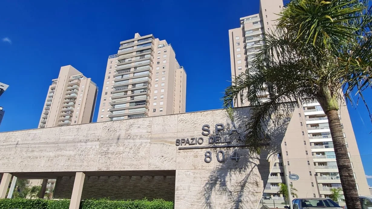 Entrada do condomínio Spazio Dell'Acqua com muro de pedra, paisagismo e torres residenciais ao fundo